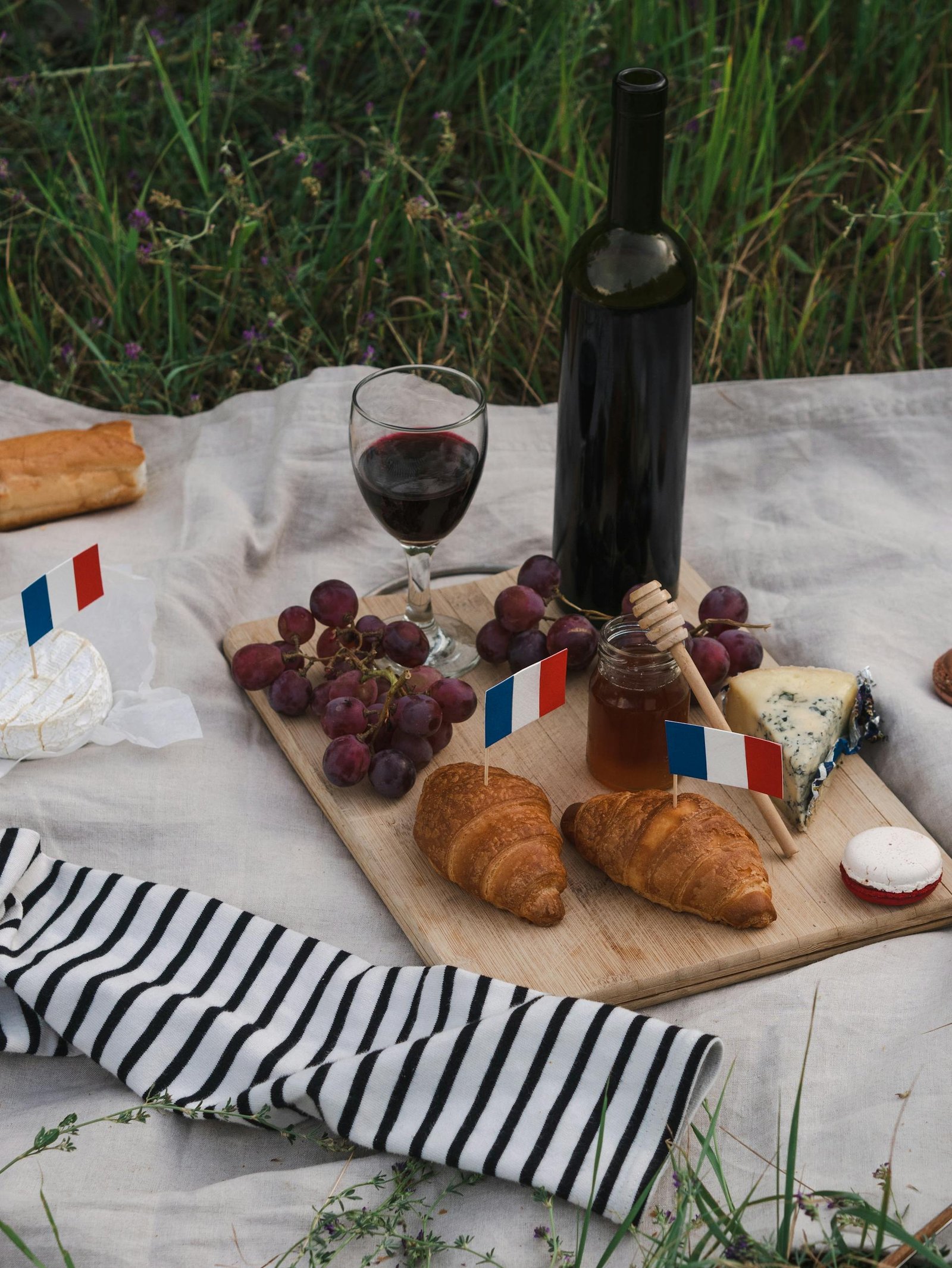 A delicious French picnic setup with wine, cheese, grapes, and pastries on a blanket.