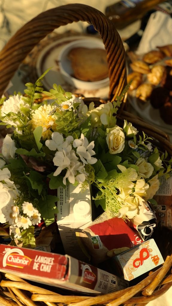 A cozy picnic basket filled with flowers and snacks, illuminated by warm sunlight.