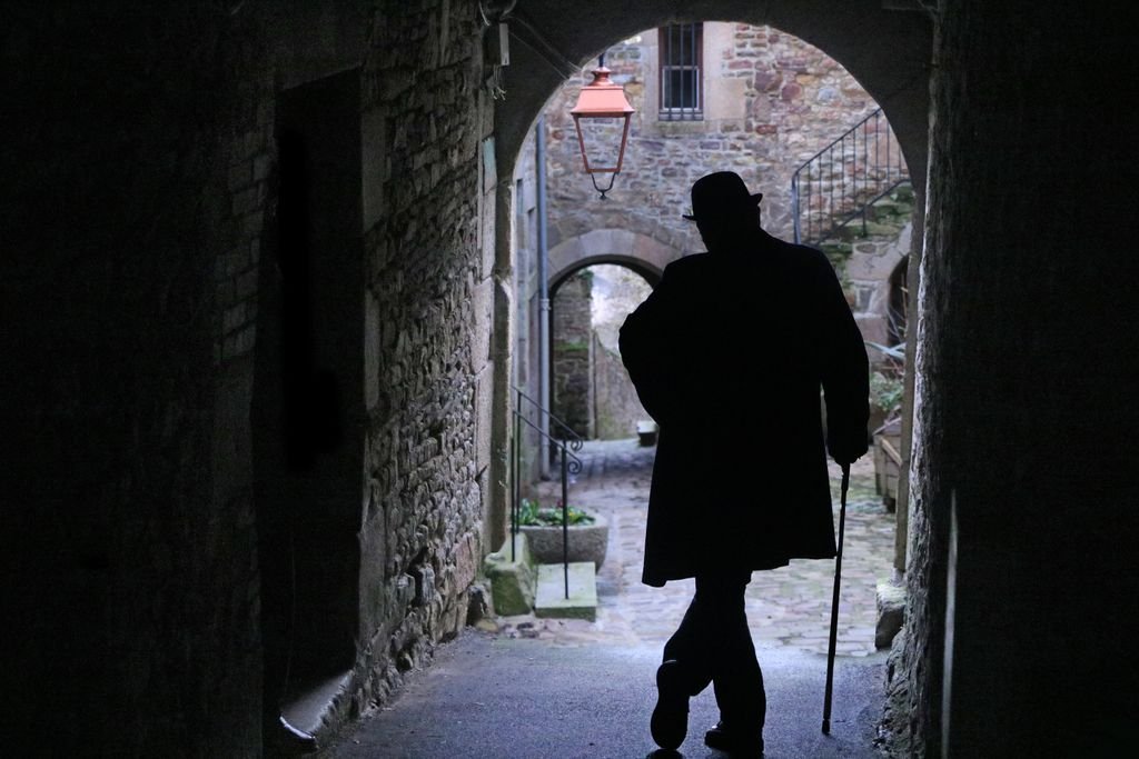 A silhouette of a man with a cane in a historic alley of Villedieu-les-Poêles, France.