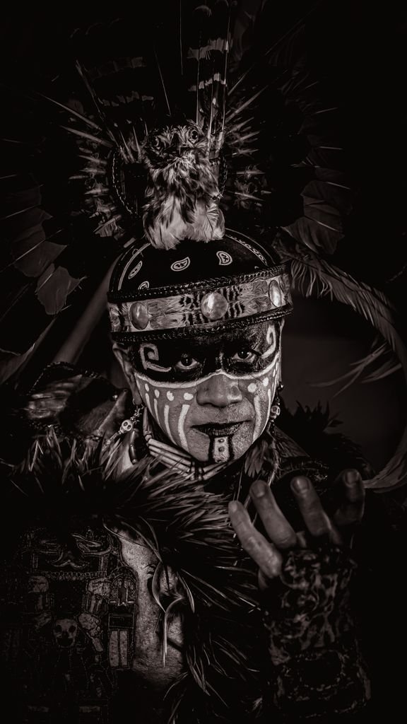 Captivating black and white portrait of a Native American in traditional attire with face paint.