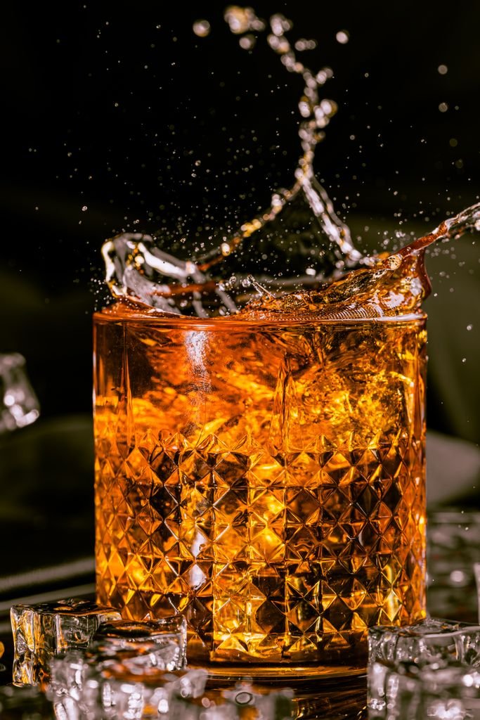 Dramatic capture of whiskey splashing in a crystal glass surrounded by ice cubes.