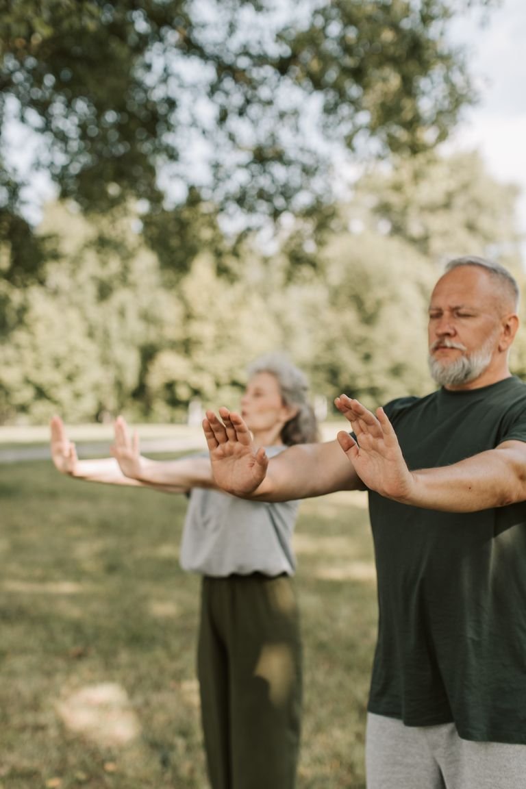 Elderly couple meditating and enjoying wellness outdoors with arms outstretched.