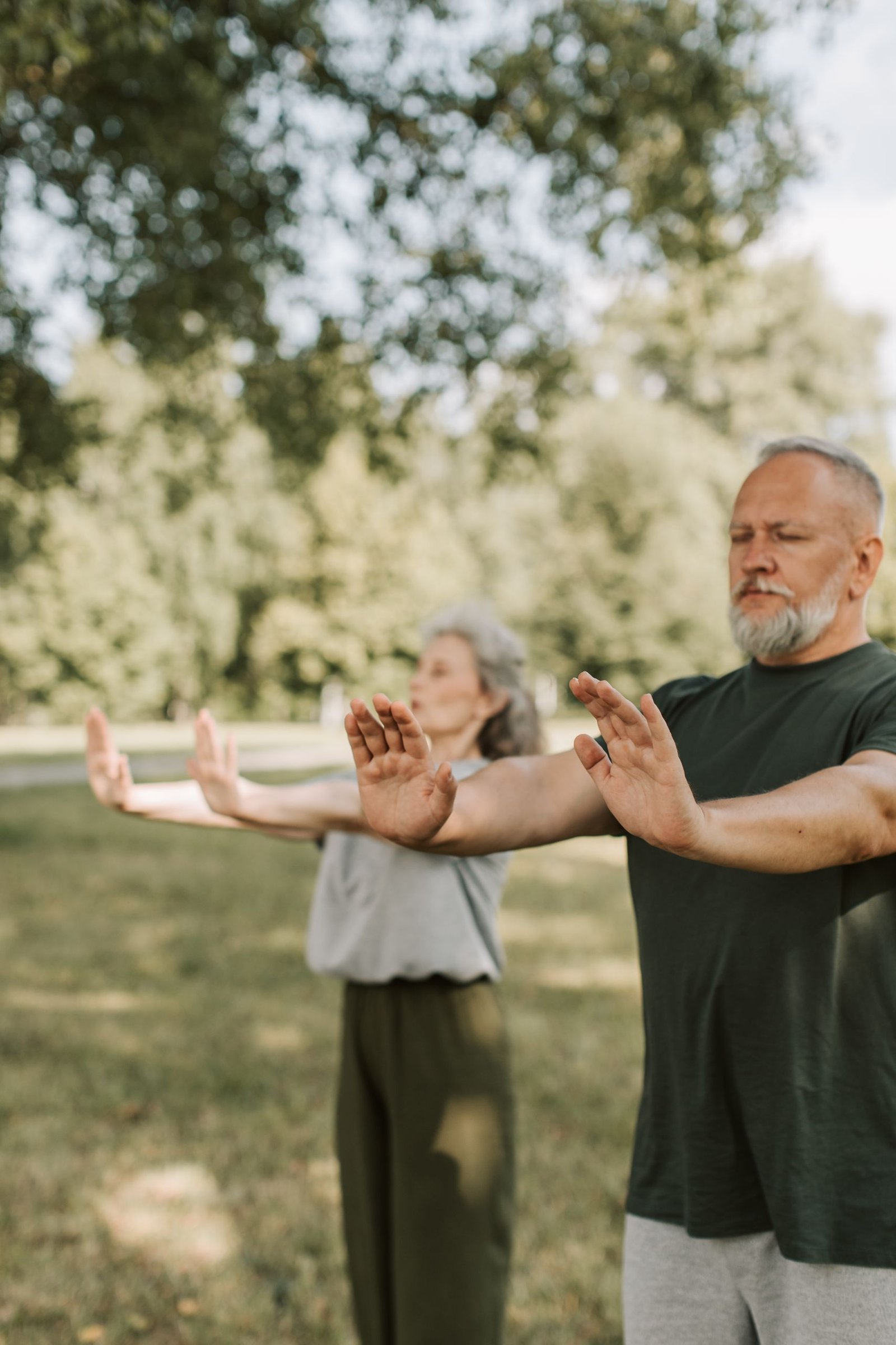 Elderly couple meditating and enjoying wellness outdoors with arms outstretched.