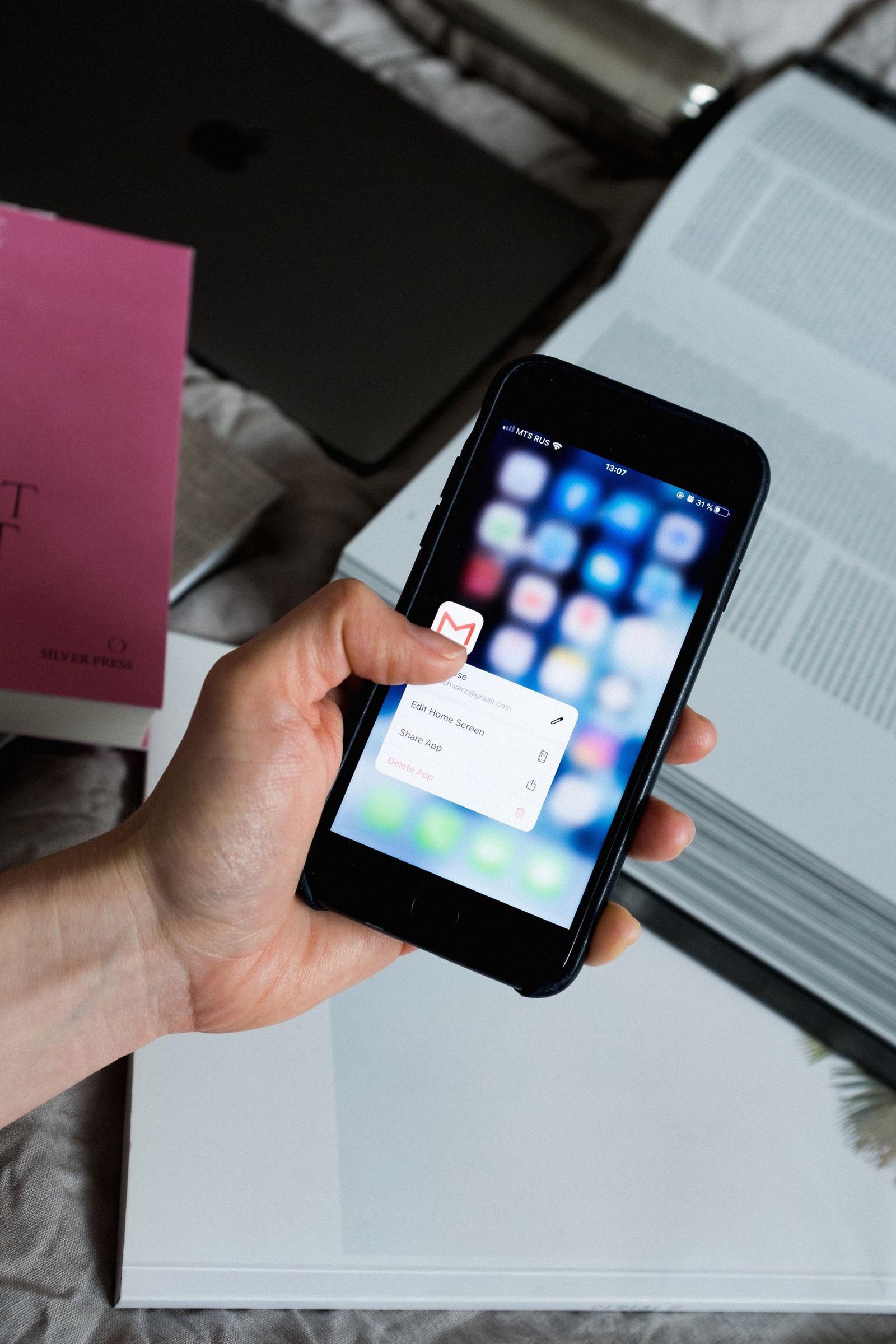 Hand holding smartphone with email app open, surrounded by books and laptop.