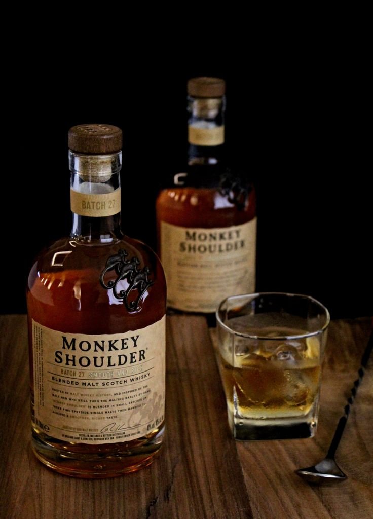 Monkey Shoulder whiskey bottles with a glass on a wooden table.