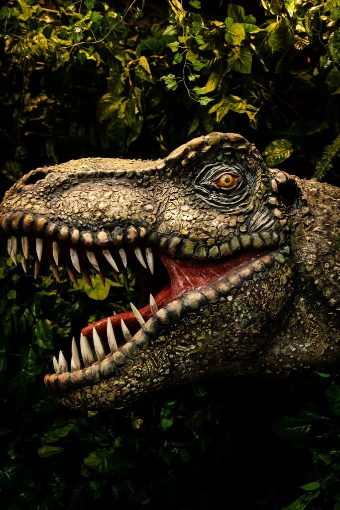 Realistic dinosaur head with open jaws surrounded by dense jungle foliage.