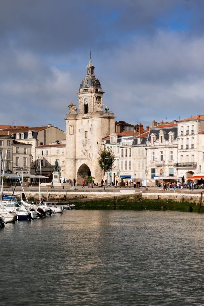 Scenic view of La Rochelle's Vieux Port with the Grosse Horloge tower, framed by cloudy skies.