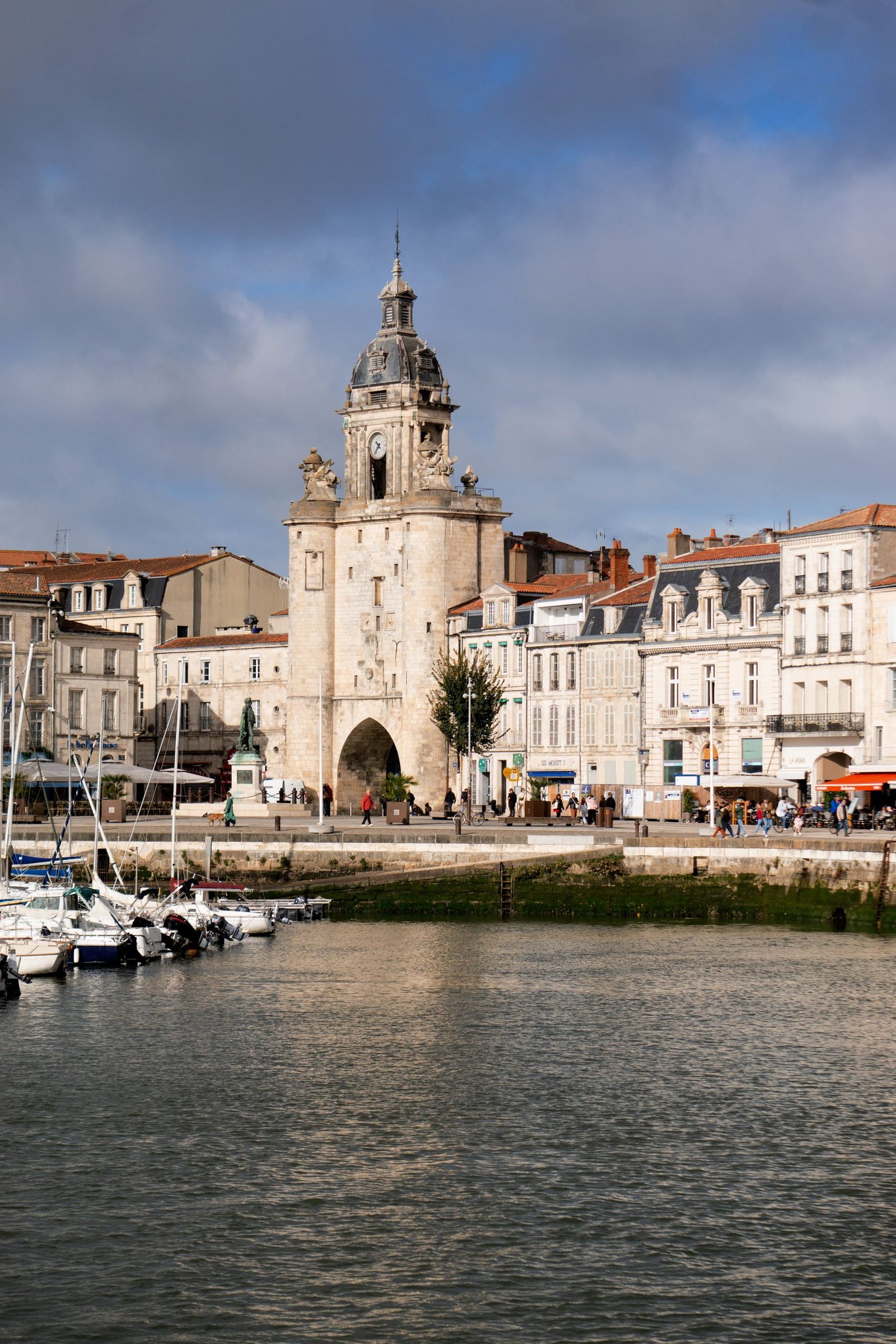 Scenic view of La Rochelle's Vieux Port with the Grosse Horloge tower, framed by cloudy skies.