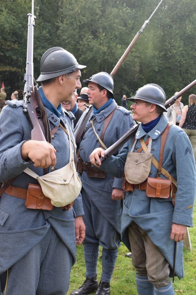 Three men in vintage military uniforms participate in a historical reenactment outdoors.