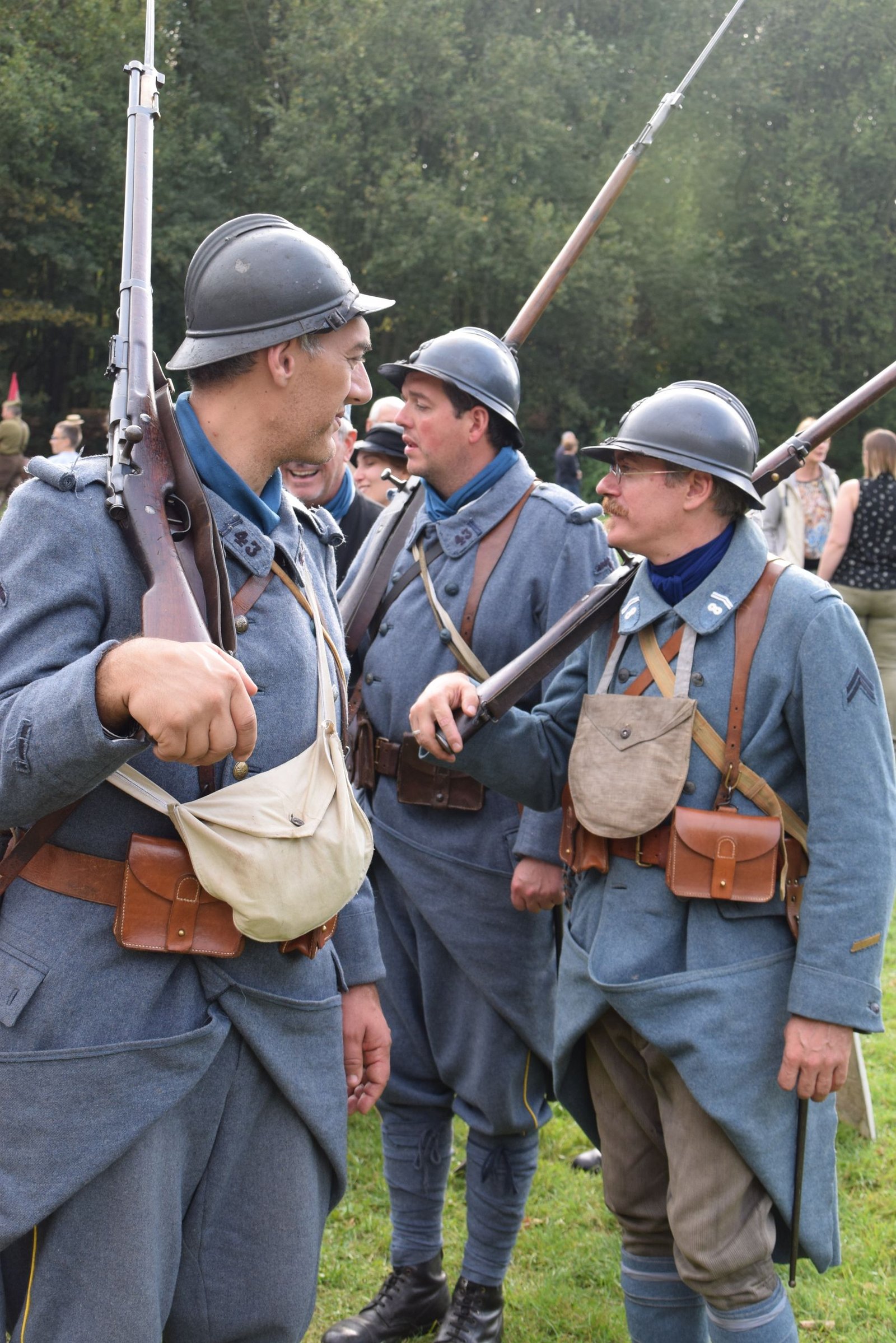 Three men in vintage military uniforms participate in a historical reenactment outdoors.