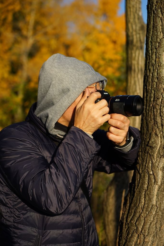 A photographer in a hoodie takes a picture outdoors during fall.