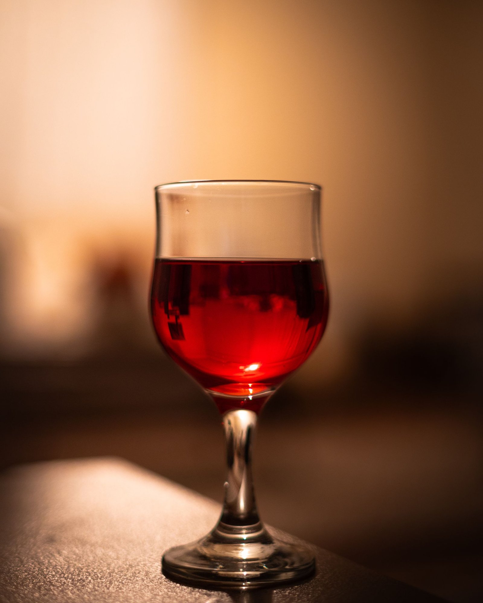 Close-up of a glass of red wine on a table with a soft bokeh background, evoking a warm and inviting atmosphere.
