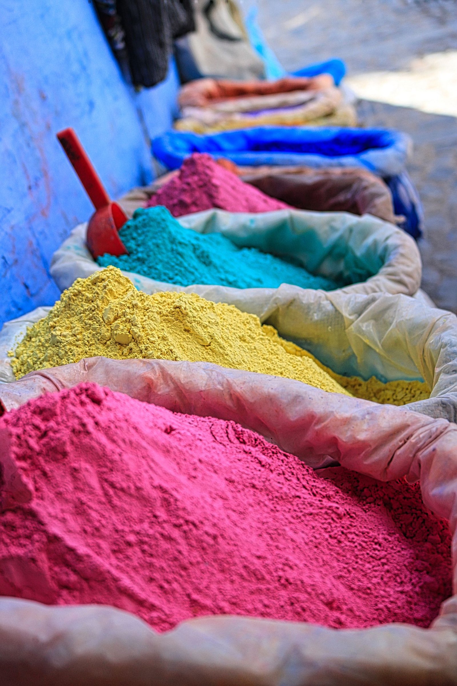 Colorful powders in sacks at a market stall. Bright pink, yellow, and blue hues.
